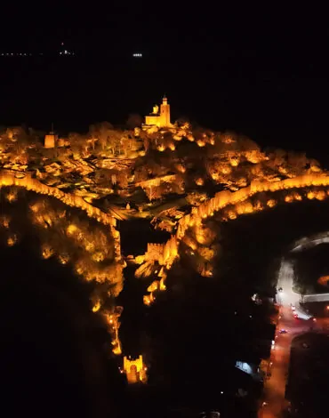 Изглед с дрон на спектакъла 'Звук и светлина' във Велико Търново, озаряващ крепостта Царевец през нощта.